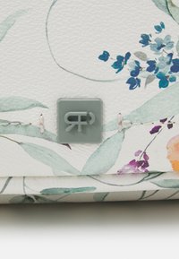Design floral sur cuir texturé blanc avec des feuilles vertes et des fleurs bleues. Emblème logo gris et détails cousus visibles.