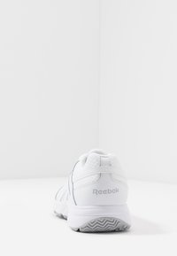 Hvid sportssko lavet af mesh og syntetisk materiale, med en dæmpet hæl, polstret krave og Reebok-logo på bagsiden.