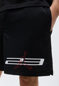Sorte mesh basketballshorts med rødt og hvidt "23" og Jumpman-logo nær kanten, vist på en person med hånden i lommen.