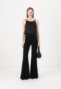Svart spaghetti-strap topp parret med høyt liv, flagrende svarte bukser. Modellen holder en liten svart håndveske. Glatt stoff med minimale detaljer.