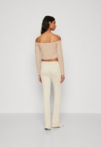 Beige off-shoulder topp med lange ermer, parret med kremfargede rillede slengbukser, som fremhever glatte teksturer og tettsittende design.