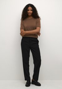 Brun kortærmet sweater parret med sorte skræddersyede bukser. Sættet har en glat tekstur og en afslappet pasform, kompletteret med sorte sko.