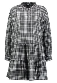 Svart och vit rutig klänning med långa ärmar, krage och flerfaldig volangnert. Tillverkad av lätt material med en mjuk textur.