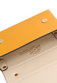 Portafoglio giallo in pelle con interni beige a contrasto, dotato di hardware dorato e di un marchio "Made in Italy" impresso.