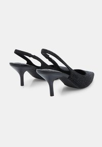 Melnas slīdošās papēžkurpes ar vidēja augstuma šauriem papēžiem un spīdīgām rhinestone rotācijām uz siksnām un augšdaļām.