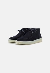 Suede ankle boots in navy blue with tonal laces, white rubber sole, and visible stitching detail along the edge. Soft texture and rounded shape.