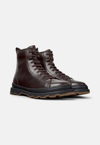 Botas de cuero marrón hasta el tobillo con un acabado suave, que cuentan con cierre de cordones, suela de goma y fondo texturizado para agarre.