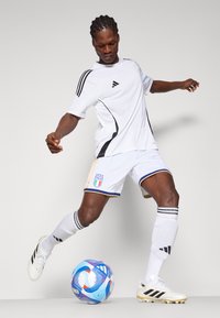 White athletic jersey with black trim, matching white shorts featuring blue and gold accents, black soccer cleats, and a multicolored soccer ball.