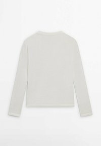 Maglia a maniche lunghe in tessuto crema chiaro. Presenta un collo rotondo, un taglio aderente e dettagli di cucitura sottili lungo le spalle e i polsini.