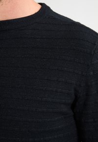 Pulover negru tricotat cu o textură cu nervuri, având striații orizontale. Decolteu rotund, material moale, design aderent.