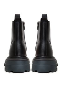 Paire de bottines noires en cuir avec semelles en caoutchouc épaisses et fermetures éclair à l'arrière, vues de dos sur fond blanc.