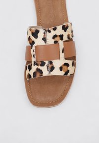 Sandalia de estampado de leopardo con una correa de cuero marrón claro, suela plana y un forro suave. Presenta un diseño de correa cruzada ancha con una textura suave.