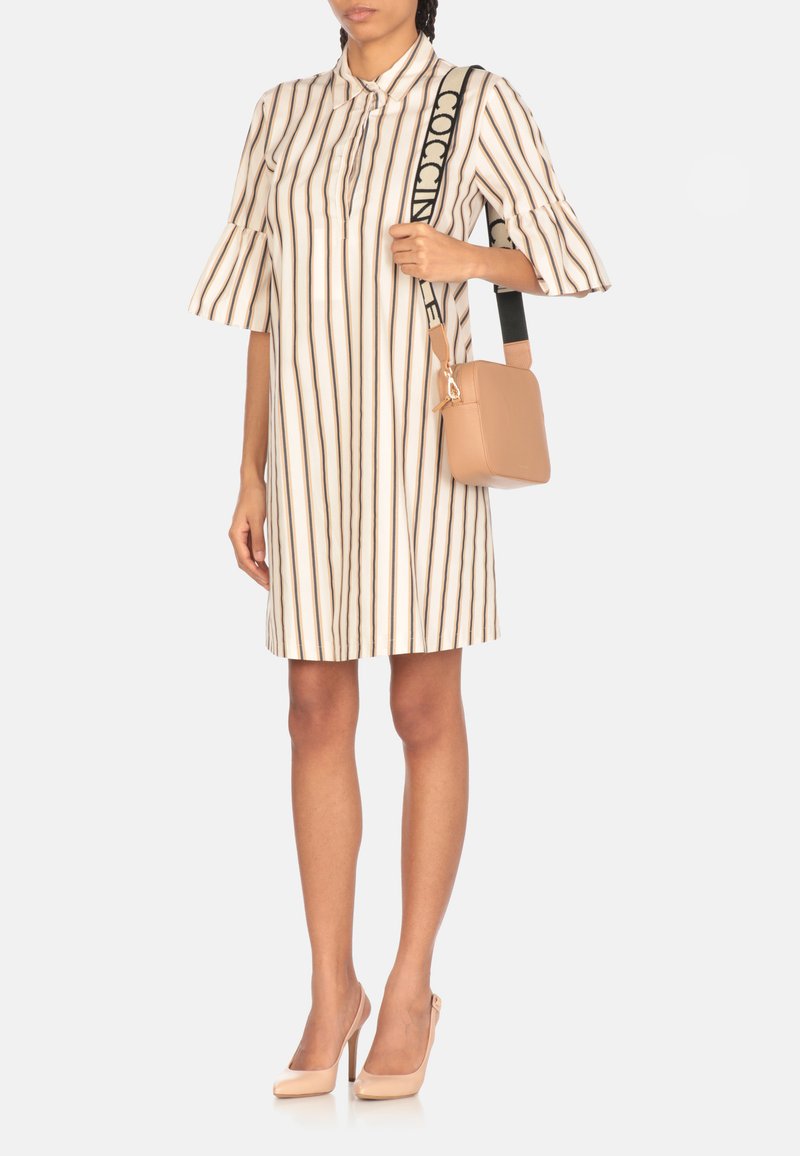 Abito camicia a righe beige con maniche svasate, abbinato a una borsa beige liscia. Modella che indossa scarpe con tacco nude.