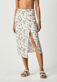 Jupe midi blanche à fleurs, ornée de fleurs roses et de feuilles vertes, avec une fente sur le côté et des accents de boutons sur le côté gauche. Le tissu est léger.