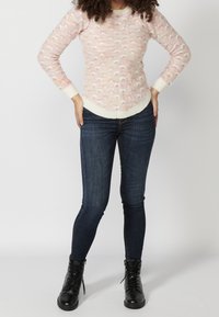 Suéter texturizado de color rosa claro con acentos crema, combinado con jeans ajustados de color azul oscuro y botas de tobillo negras con cordones.