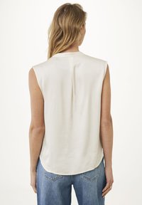 Ärmlös blus i krämfärg, tillverkad av ett slätt tyg, med en veck bak och en rundad nederkant. Matchad med ljus tvättade denimjeans.