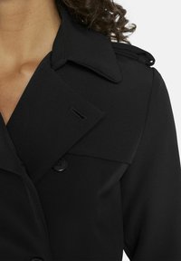 Zwarte trenchcoat met een brede kraag, twee knopen en een gladde, matte textuur met subtiele stikseldetails.