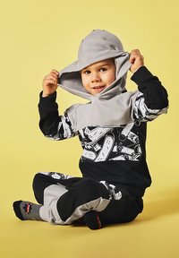 Dziecięcy dres w kolorze czarnym z szarymi akcentami. Posiada kaptur oraz grafikę z deskorolkami. Gładki materiał, luźny krój i elastyczne mankiety.