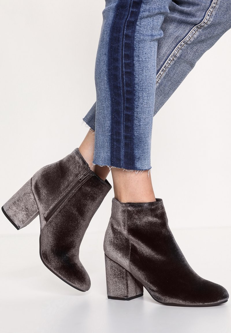 Botines de terciopelo gris oscuro con un alto tacón cuadrado y una cremallera lateral. La textura suave y la silueta elegante tienen un aspecto moderno y refinado.