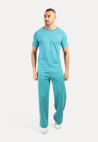 T-shirt turchese a maniche corte e pantaloni ampi coordinati, realizzati in un tessuto morbido, con un discreto logo sul petto.