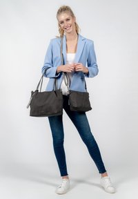 Schwarze Stoffhandtasche mit zwei Schulterriemen, glatter Textur, dezentem Markenlogo, kombiniert mit hellblauem Blazer und blauen Jeans.