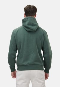 Felpa con cappuccio verde realizzata in morbido cotone misto, caratterizzata da una vestibilità comoda e polsini a costine. La parte posteriore ha una texture liscia e senza loghi visibili.