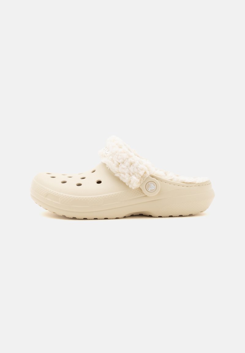 Sabot beige à enfiler avec des trous de ventilation et une doublure blanche duveteuse autour du col du talon, présenté en vue latérale sur un fond uni.