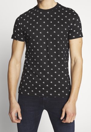 Zwart T-shirt met korte mouwen van zacht katoen, met een patroon van herhaalde witte CK-logo's over het hele shirt. Getailleerd model, ronde hals.