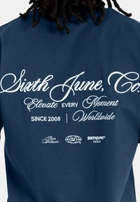 Camiseta de algodón azul marino con texto en blanco, gráficos de logotipo y acentos que dicen "Sixth June, Co." y "Desde 2008."