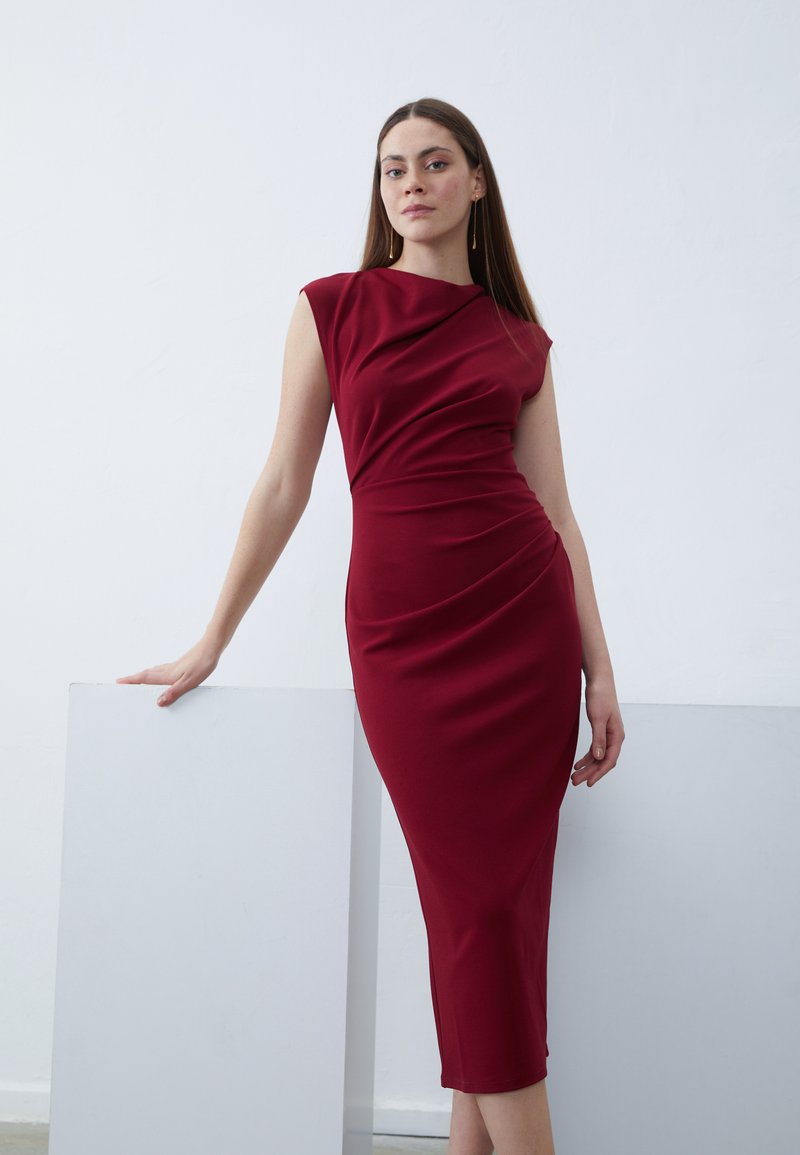 Red fitted dress with a draped neckline, cap sleeves, and a knee-length hem. Smooth, stretchy fabric highlights body contours.