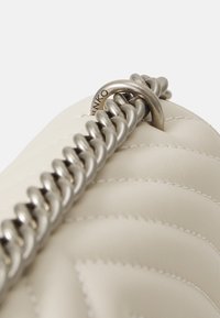 Borsa in pelle cream trapuntata con manico a catena argentata e un accento a cerchio in metallo. Dettagli cuciti lungo la superficie della borsa.