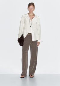 White silk blouse with long sleeves, paired with loose brown trousers. Accessorized with a dark brown handbag and a simple necklace.