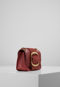 Röd läderhandväska med en avslappnad form, utmärkt av en framträdande guldfärgad detaljer och en texturerad klaff. Kedjestropp ingår.