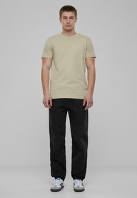 Tricou bej cu mânecă scurtă și decolteu rotund, purtat cu blugi negri drepți și pantofi sport albi cu accente gri și albastre.