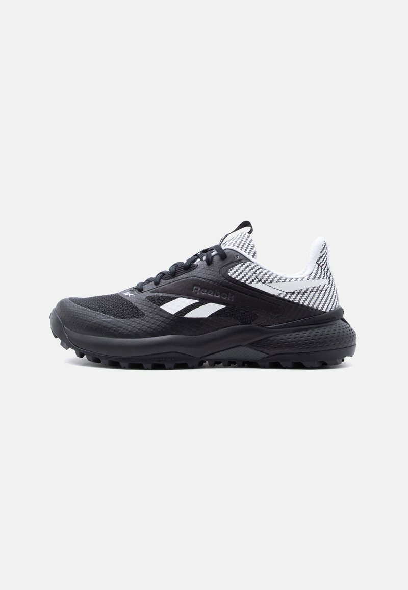 Αθλητικό παπούτσι Reebok σε μαύρο και άσπρο με υφή σόλας και υφασμάτινο κολάρο με σχέδιο, εμφανίζεται από την εξωτερική πλευρά σε απλό φόντο.