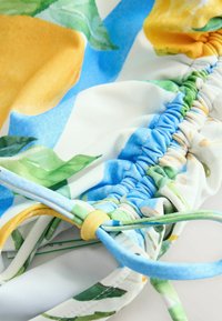 Blumiger Stoff mit gelben Zitronen und grünen Blättern auf weißem Hintergrund. Strukturierter, geraffter Entwurf mit blauen und gelben Akzenten.