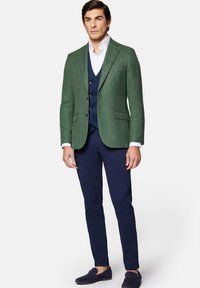 Zielony blazer o fakturze, granatowa kamizelka, biała koszula, granatowe spodnie, niebieskie mokasyny. Slim fit, jednozapięciowy design z dwoma guzikami.