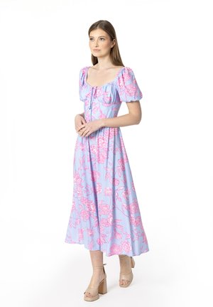 Blauwe bloemenjurk met korte opgezette mouwen en vierkante hals. Heeft roze bloemenpatronen en een vloeiende A-lijn silhouet. Tan platform sandalen.