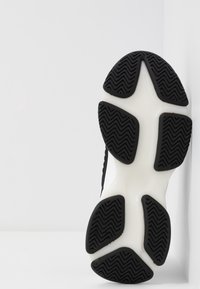 Semelle de chaussure de sport noir et blanc avec un motif texturé en zigzag sur le caoutchouc noir et une semelle intermédiaire blanche lisse.