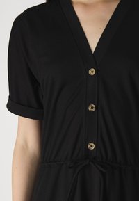 Vestido preto de manga curta com decote em V, apresentando um fecho com botões na parte da frente e uma cintura ajustável com cordão, feito de um tecido suave e leve.