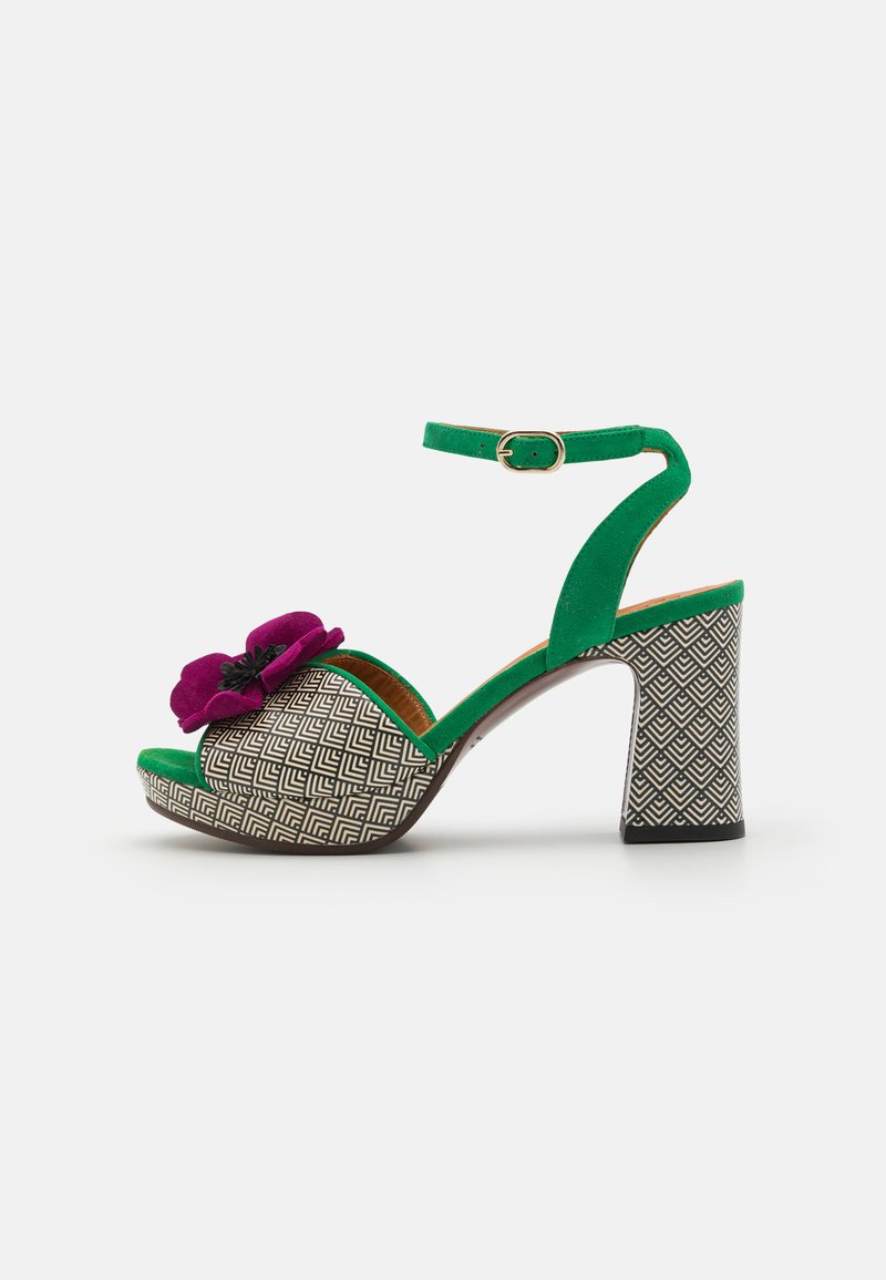 Green suede high-heeled sandal with black and white geometric patterned base, featuring a purple flower accent on the front and an ankle strap.