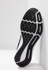 La semelle de la chaussure présente un design en caoutchouc noir texturé avec des motifs hexagonaux, des lignes d'accentuation blanches et une forme courbée, ergonomique.