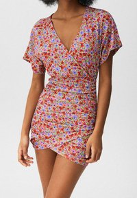 Vestido envolvente floral en rojo con flores moradas y azules; mangas cortas; ajuste entallado con textura fruncida en la cintura; escote en forma de v.