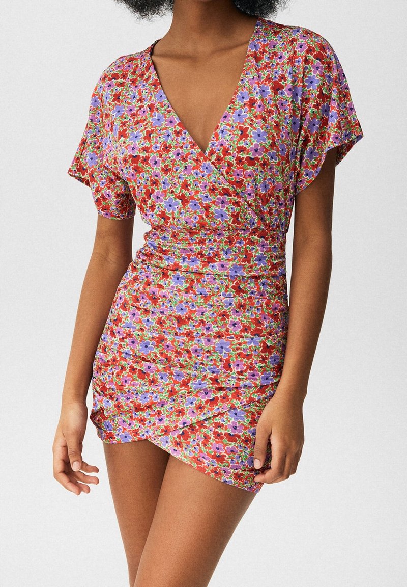 Vestido envolvente floral en rojo con flores moradas y azules; mangas cortas; ajuste entallado con textura fruncida en la cintura; escote en forma de v.