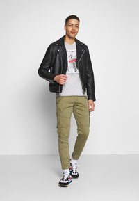 Zwarte leren motorjack, grijs graphic t-shirt, olijfgroene cargobroek en multicolore sneakers. Rechte pasvorm met ritsen en zakken.
