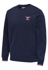 Sweat-shirt à col rond bleu marine avec logo Hummel rouge et blanc sur la poitrine, et poignets côtelés avec détail de rayures rouges et blanches.