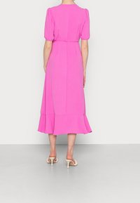 Vestido midi rosa con mangas abullonadas, cintura ceñida con cinturón y dobladillo acampanado. Textura suave, diseño sencillo y sin patrones visibles. Combinado con tacones neutros.
