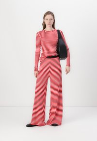 Langärmliges Oberteil mit rot-weißen Streifen und weit geschnittene Hose, kombiniert mit einer schwarzen Tasche. Das Outfit hat eine lässige Passform und eine glatte Textur.