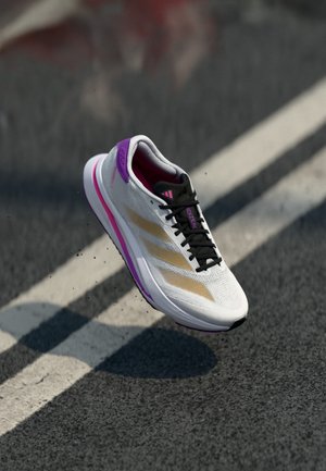 Weißer leichter Laufschuh mit pinken und goldenen Akzenten, strukturiertem Mesh-Obermaterial, schwarzen Schnürsenkeln und einer gepolsterten Sohle für zusätzlichen Komfort.