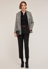 Blazer grigio a quadri con bordi sfrangiati, blusa nera a coste, pantaloni neri e stivaletti neri, abbinato a una piccola borsa nera.